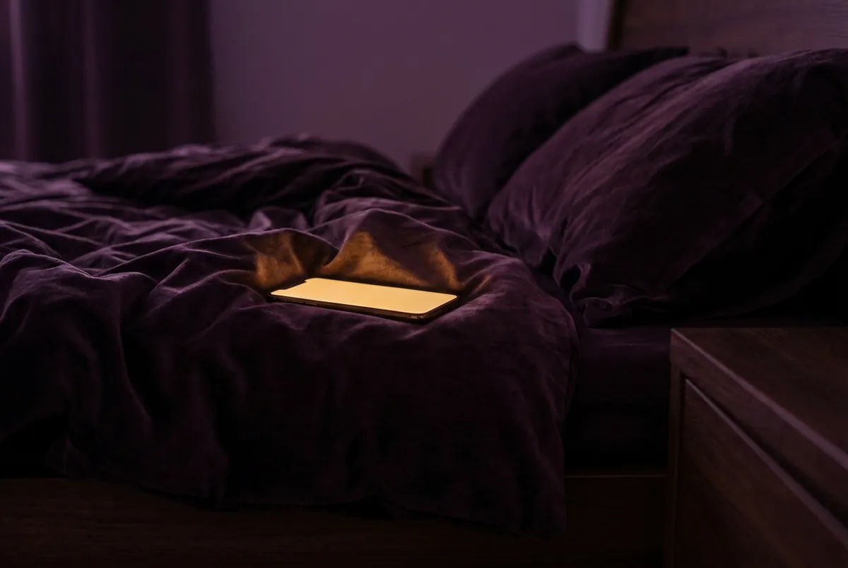 Ein Handy liegt leuchtend auf einem dunklen Bett