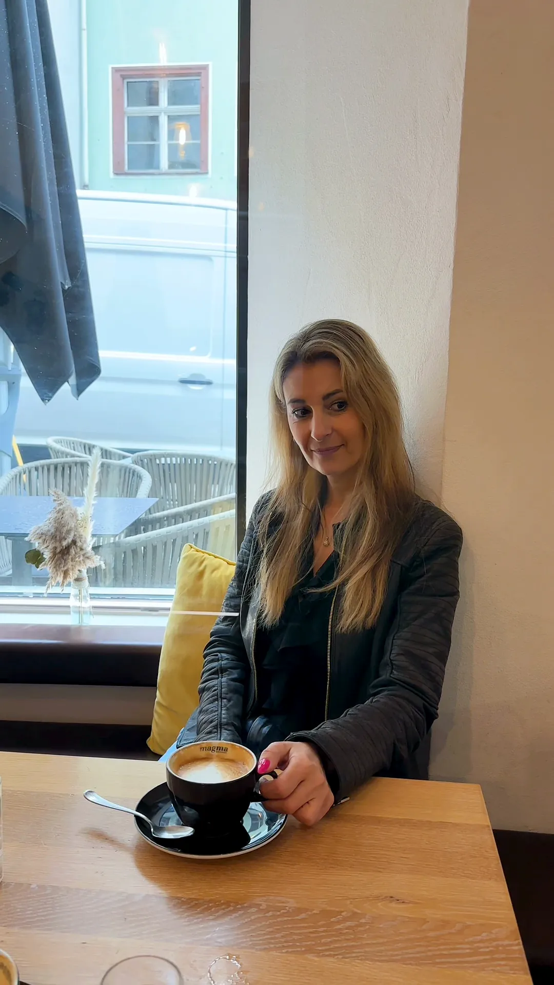 Susanne sitzt allein im Café am Fenster, vor ihr ein Cappuccino